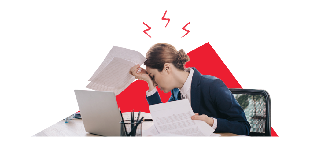 Colleague at a desk, head in hands, with stacks of work and an open laptop in front of her.